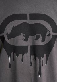 Dark gray T-shirt featuring a large black rhino graphic, with trailing black paint drips. Soft fabric with a classic crew neck design.