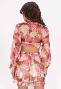 Conjunct vestimentar în două piese cu model floral, compus dintr-un top scurt cu mâneci lungi și o fustă. Fabricat dintr-un material transparent cu margini volan și culori vibrante.
