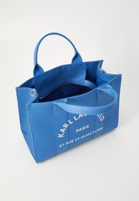 Borsa a tramolla blu in canvas con manici superiori doppi, tasca interna con zip e testo bianco con il nome del marchio e l'indirizzo sul pannello frontale.
