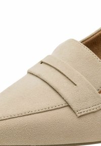 Mocassin en daim beige avec une bride cousue sur le dessus et un bout lisse légèrement pointu.