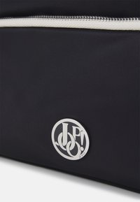 Borsa in tessuto nero con superficie testurizzata, dotata di una cerniera bianca e di un logo circolare argentato con lettere intrecciate.