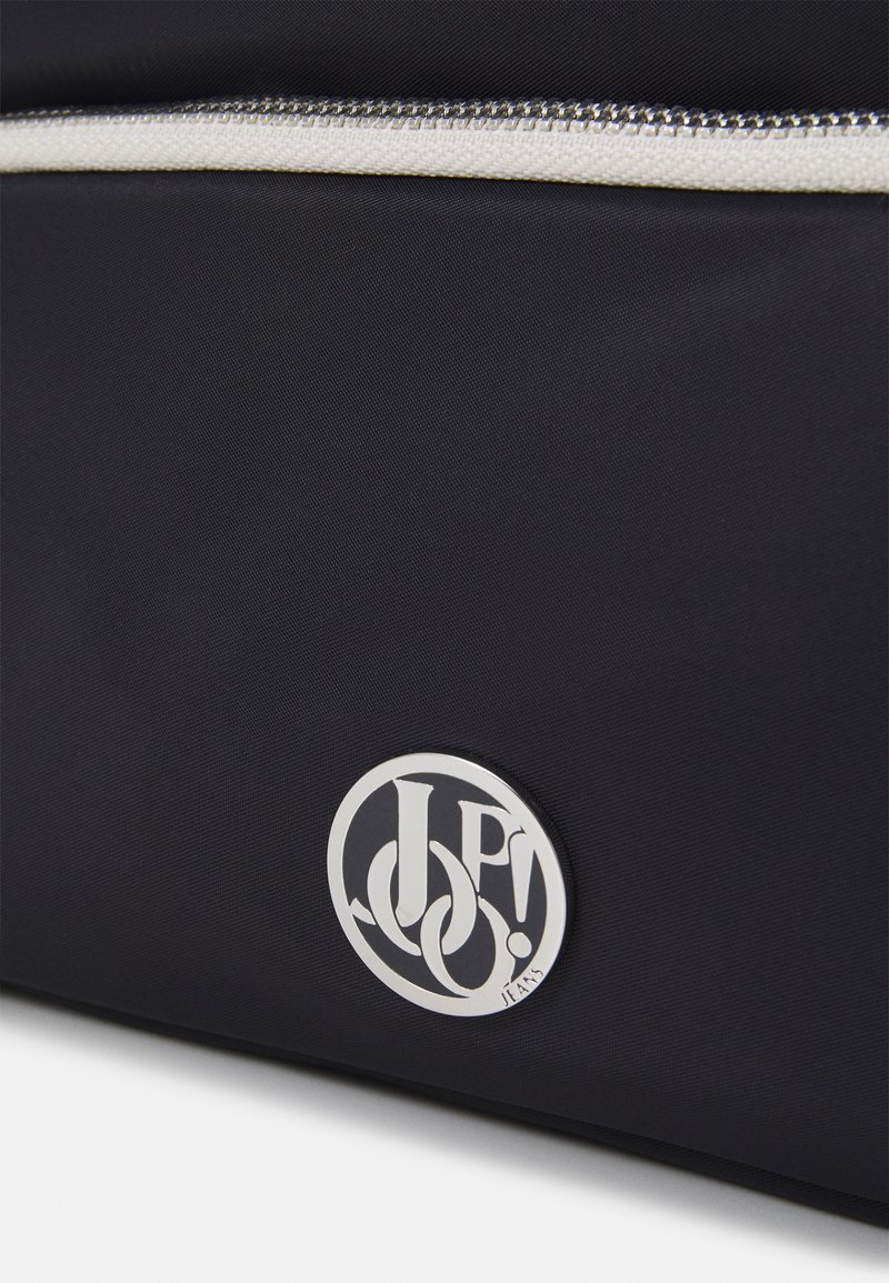 Schwarze Stofftasche mit strukturierter Oberfläche, ausgestattet mit einem weißen Reißverschluss und einem runden silbernen Logo mit ineinander verschlungenen Buchstaben.