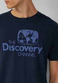 Granatowa bawełniana koszulka z jasnoniebieską grafiką globu i napisem "KANAŁ ODKRYĆ" poniżej, z okrągłym dekoltem.