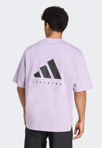 Fialové oversized tričko s krátkými rukávy, na zádech s velkým černým geometrickým logem a slovem "TRÉNINK".