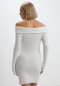 Abito bianco off-the-shoulder con texture a coste, maniche lunghe e design aderente. Tessuto liscio con un taglio a metà coscia.