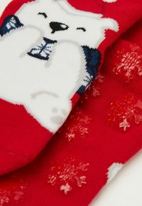 Calzini rossi con disegno di un orso polare bianco. Le suole sono decorate con motivi a fiocco di neve in gomma texturizzata, che migliorano la presa e i dettagli.