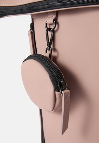 Rožinė aksesuarų dėžutė, pagaminta iš lygios medžiagos, su juoda užtrauktuku ir hardware užsegimu, pritvirtinta prie didesnės maišelio naudojant spaustuką.
