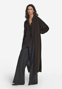 Lång svart cardigan över en mörk blus och vida grå byxor. Cardiganen har öppna sidor och en avslappnad passform, med mjukt material.