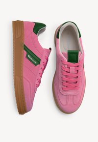 Růžové semišové tenisky se zelenými detaily, s masivní béžovou gumovou podrážkou a šněrováním. Název značky je na boku zobrazený bílou barvou.