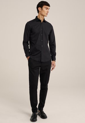 Chemise noire à boutons en coton lisse, avec un col classique et des manches longues. Assortie à un pantalon noir et des chaussures à enfiler.