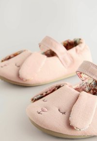 Chaussons en tissu rose avec un design de lapin, featuring des oreilles en tissu, des détails de visage brodés et une doublure à motifs floraux. Fermeture à bande Velcro.