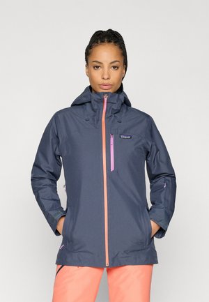 Casaco azul-marinho resistente à água com capuz, apresentando um fecho rosa e detalhes em rosa, punhos ajustáveis e bolsos frontais. Textura suave, design moderno.