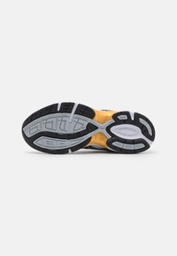 Semelle d'une chaussure de sport avec des bandes de caoutchouc noires, grises, blanches et jaunes conçues pour la traction et la flexibilité.