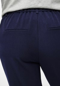 Jūras zilas bikses ar gludu tekstūru, ar elastīgu jostu un divām aizmugures kabatām. Vienkāršs, pielāgots dizains un elegants apdare.