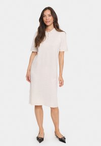 Ljusbeige polo klänning gjord av mjukt tyg. Kort ärm, knapplist, knä-lång, med sidoklyftor. Parat med svarta spetsiga ballerinas.