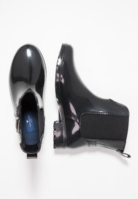 Botas de lluvia negras hasta el tobillo con un acabado brillante, paneles laterales elásticos, suelas de goma texturizadas y lengüetas de agarre para facilitar el uso.