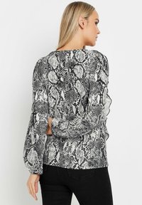 Blusa con stampa serpente bianca e nera, maniche lunghe a sbuffo, texture liscia e dettagli arricciati lungo le maniche.