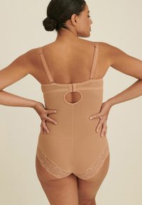 Beige bodysuit met kantafwerking, heeft verstelbare banden en een cirkelvormige uitsnijding op de rug. Glad textuur met een getailleerd ontwerp.