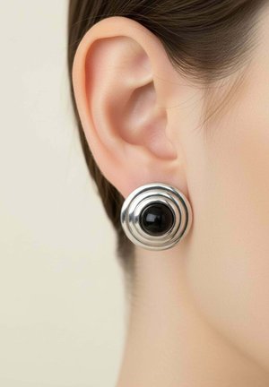 Közeli kép egy személy füléről, aki kerek ezüst fülbevalót visel fekete középpel és koncentrikus körös mintával.