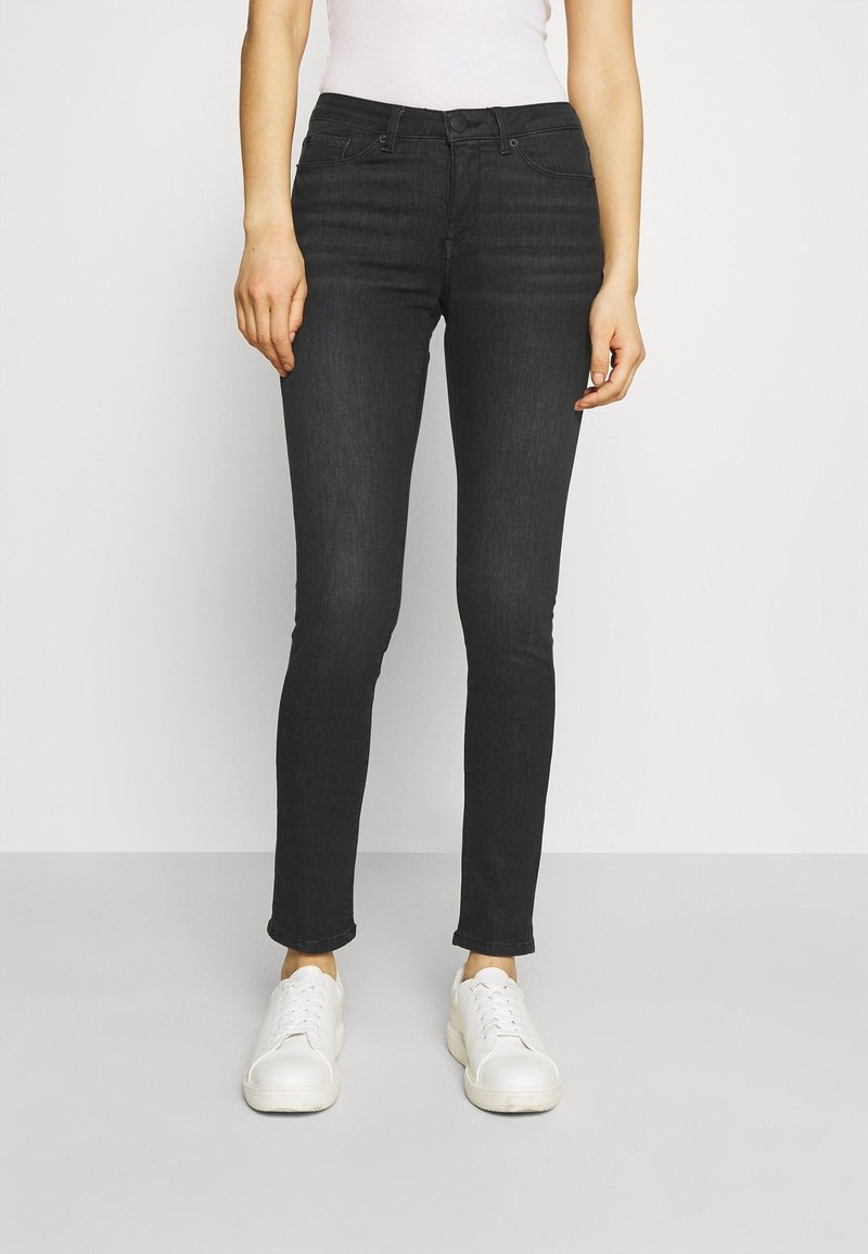 Mustat slim-fit farkut, jotka on valmistettu denimestä, klassisella viiden taskun designilla ja hienovaraisella haalistuneella pinnalla, yhdistetty valkoisiin lenkkitossuihin.