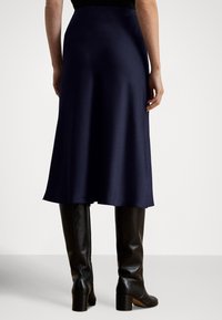 Tengerészkék szatén midi szoknya, folyékony eséssel, sima textúrával és enyhén bővülő szegéllyel. Térdig érő fekete bőr csizmával párosítva.