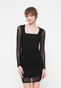 Rochie neagră cu decolteu pătrat, mâneci lungi din material transparent, textură plisată și o siluetă ajustată care se termină deasupra genunchiului.