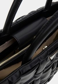 Bolso Tote de cuero negro con textura trenzada, doble asa superior, detalle de cremallera dorada y forro interior de tela beige.