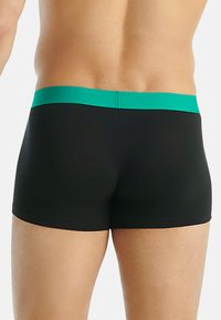 Musta uimapuku, jossa on teksturoitu vihreä vyötärö, vartalonmyötäinen muotoilu ja lyhyet lahkeet. Kangas näyttää sileältä ja joustavalta.