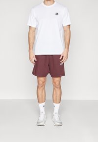 Vit kortärmad T-shirt med svart logotyp, vinröda träningsshorts, vita strumpor och ljusgrå sneakers. Enkel, aktivwear-design.