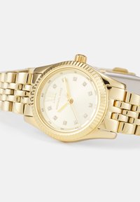 Goldfarbene Armbanduhr mit rundem Gehäuse, strukturiertem Lünette und polierter Band. Das Ziffernblatt hat ein hellgoldenes Design und diamantähnliche Stundenmarkierungen.