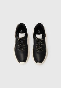 Baskets noires avec une tige en cuir texturé, des lacets accentués de doré et des semelles en caoutchouc crème. Présente un logo sur la languette et sur le côté.