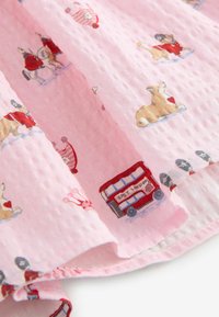 Tela rosa suave con estampados temáticos de Londres que incluyen autobuses de dos pisos rojos, corgis con sombreros y guardias con uniformes rojos.