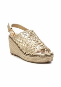 Sandalia de cuña con un diseño de crochet dorado, puntera abierta y tira trasera. Presenta un tacón envuelto en yute texturizado y un acabado metálico.