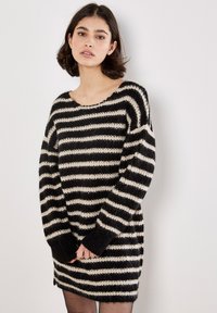 Stribet sweaterkjole i sort og creme med løs pasform, bred halsudskæring og lange ærmer. Struktureret strikmateriale med ribkantede manchetter.