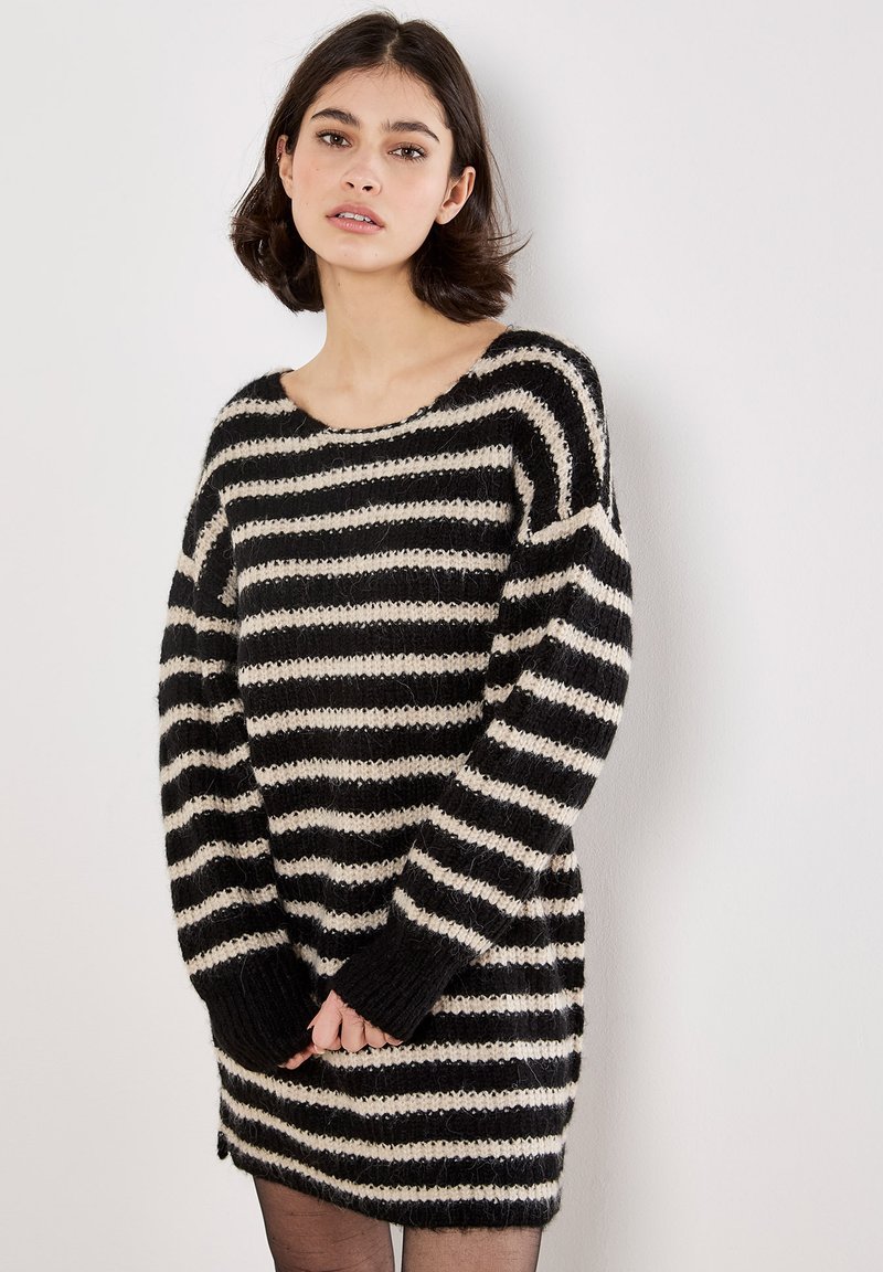 Stribet sweaterkjole i sort og creme med løs pasform, bred halsudskæring og lange ærmer. Struktureret strikmateriale med ribkantede manchetter.