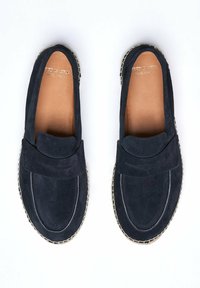 Tmavě modré semišové mokasíny s hladkou texturou, s designem na nazouvání a bílým prošitím podél okraje. Viditelná kožená stélka.
