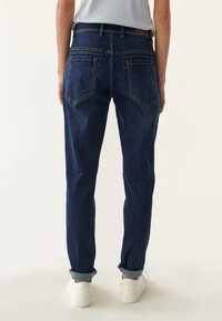 Jeans de mezclilla azul oscuro con un ajuste de pierna recta, que cuentan con dos bolsillos traseros y puños doblados. Cosidos con hilo de color amarillo en contraste.