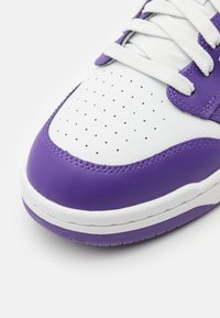 Weiße Sneaker mit lila Akzenten, aus glattem Leder, mit durchlöchertem Zehenbereich, weißen Schnürsenkeln und einer strukturierten Gummisohle.