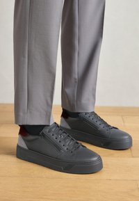 Adidași negri cu un material texturat, având un fermoar pe lateral și accente contrastante gri și bordo. Talpă groasă din cauciuc și șireturi.