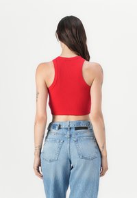 Haut court rouge à côtes avec un col rond, design ajusté. Associé à un jean taille haute bleu clair avec des poches arrière. Style minimaliste.
