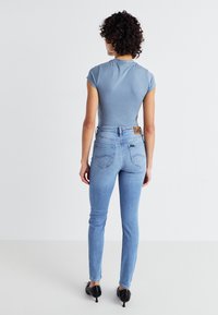 T-shirt ajusté bleu clair avec des manches courtes, associé à un jean skinny délavé clair comportant des poches arrière et un patch en cuir tan de marque.