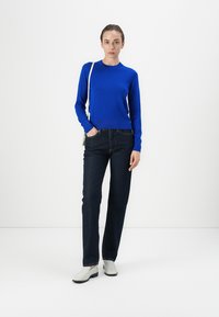 Pulover tricotat albastru cu mâneci lungi, asortat cu blugi negri din denim și pantofi gri deschis. Design simplu pe un fundal alb.
