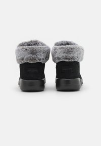 Bottines en suede noir avec un revers en fausse fourrure grise, dotées d'une semelle en caoutchouc noir et d'une branding minimaliste sur le talon.