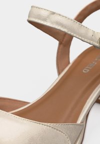 Κοντινό πλάνο λουριού σανδαλιού από μπεζ δέρμα και μαλακό πέλμα με ορατή ραφή και μερικό κείμενο της μάρκας στο πέλμα.