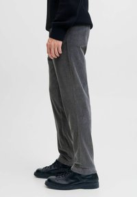 Graue Cordhosen mit vertikalen Rillen, gerader Schnitt, Seitentaschen, kombiniert mit schwarzen Schnürschuhen und einem strukturierten schwarzen Pullover.
