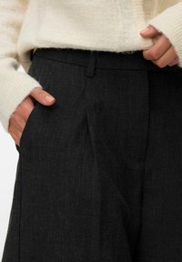 Mørk grå bukser med et teksturert stoff, med rett snitt og en sidelomme. Kombinert med en kremfarget, fluffy strikkegenser.