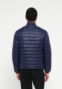 Granatowa pikowana kurtka puchowa z poziomym przeszyciem, wysokim kołnierzem i gładką fakturą. Kurtka ma długie rękawy oraz elastyczne mankiety.