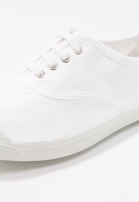 Sneaker bianca in tela con cinque occhielli metallici, design con lacci, upper testurizzato e suola in gomma con un motivo discreto.