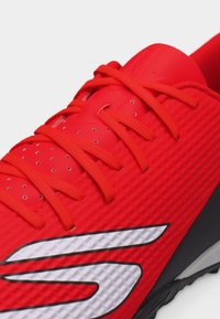 Κοντινή λήψη ενός κόκκινου αθλητικού παπουτσιού με κόκκινα κορδόνια και λευκό στυλιζαρισμένο λογότυπο στο πλάι.