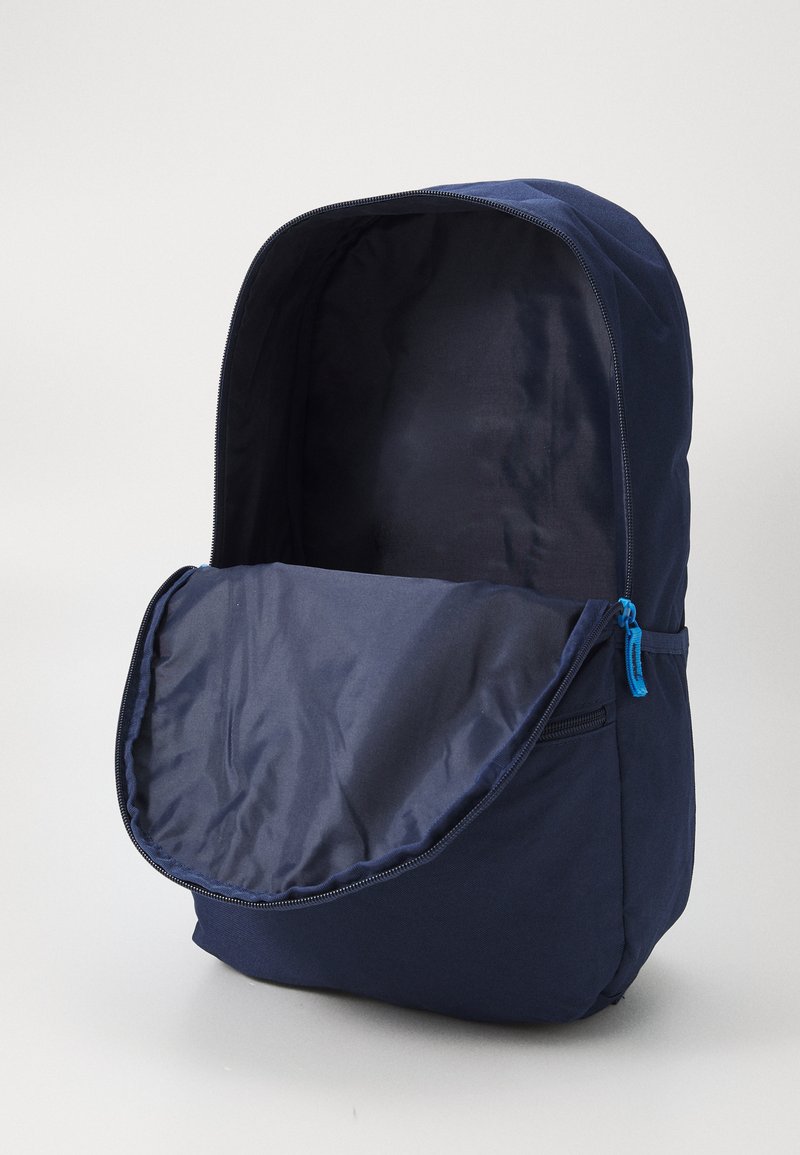 Mochila navy con un acabado mate y suave, que presenta una abertura grande con cremallera y un pequeño bolsillo lateral con una cremallera azul. El interior también es de color navy.